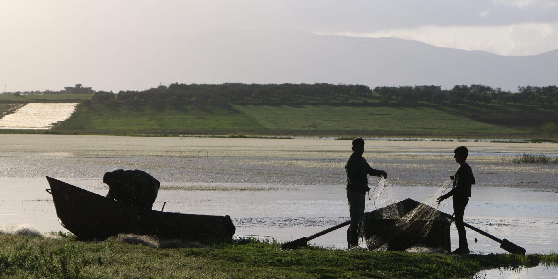 the silhouettes of two fishermen and their boat in front of a lake, in the light of dusk