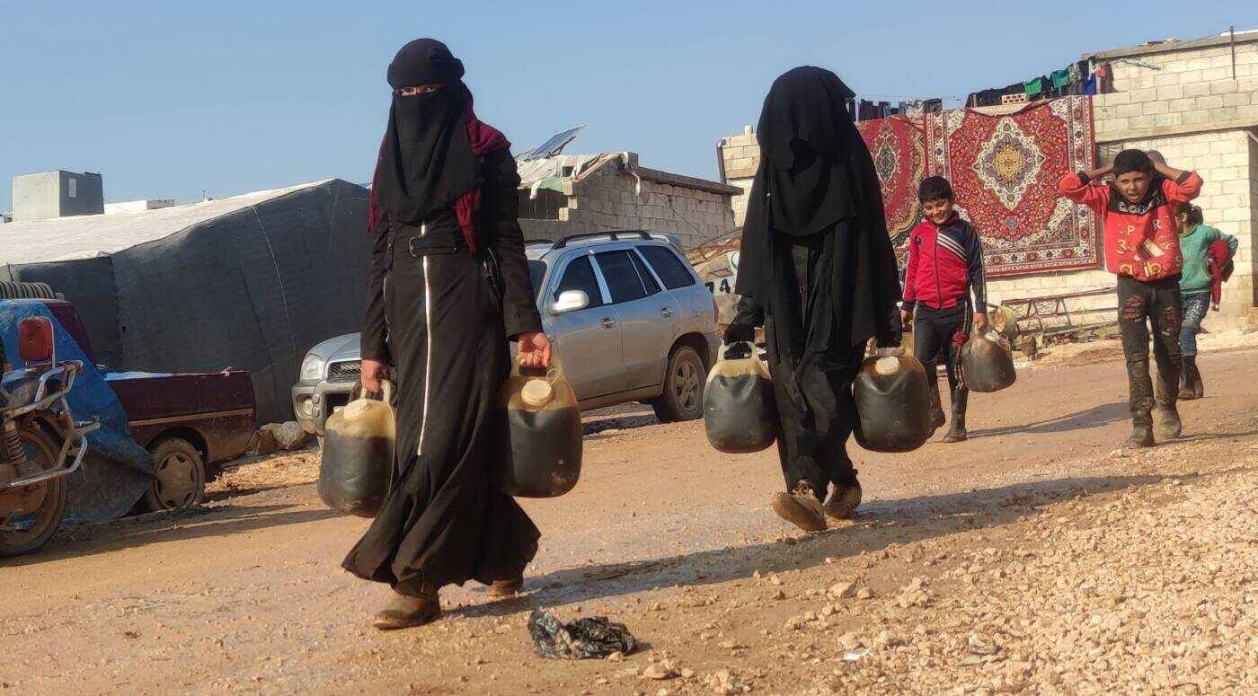 نساء وأطفال يحملون عبوات مملوءة بالمازوت المهرب في منطقة أطمة بريف إدلب الشمالي، 17/ 12/ 2021 (سوريا على طول)
