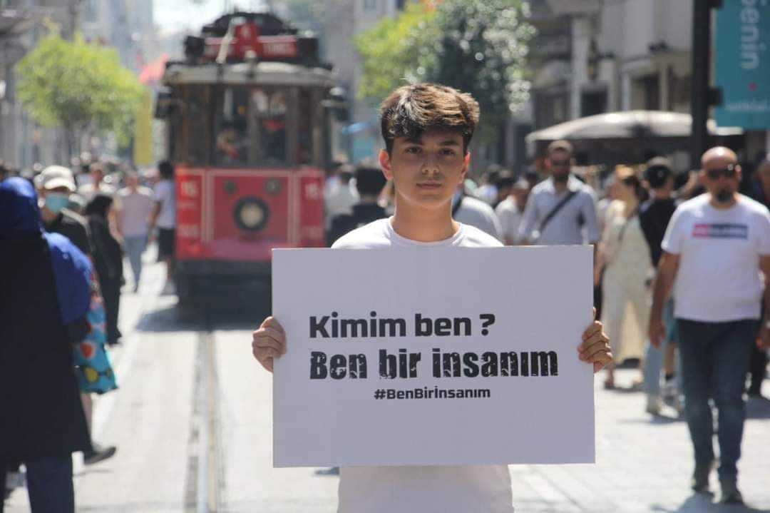 شاب تركي يرفع لافتة في مدينة اسطنبول التركية تضامناً مع الفتى السوري أحمد كنجو، كتب عليها: "من أنا؟ أنا إنسان"، 21/ 7/ 2022 (أنترنت)