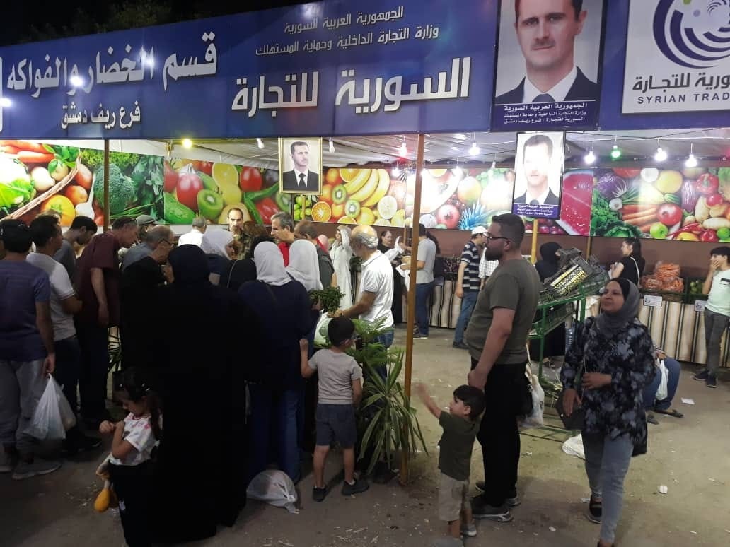 Syrians stand in front of a branch of the Syrian Trade Institution—the accredited state body that distributes subsidized goods in regime-controlled areas—during the 147th monthly “Made in Syria” shopping festival in Jaramana, Reef Dimashq, 19/7/2023 (Syrian Trade Institution)