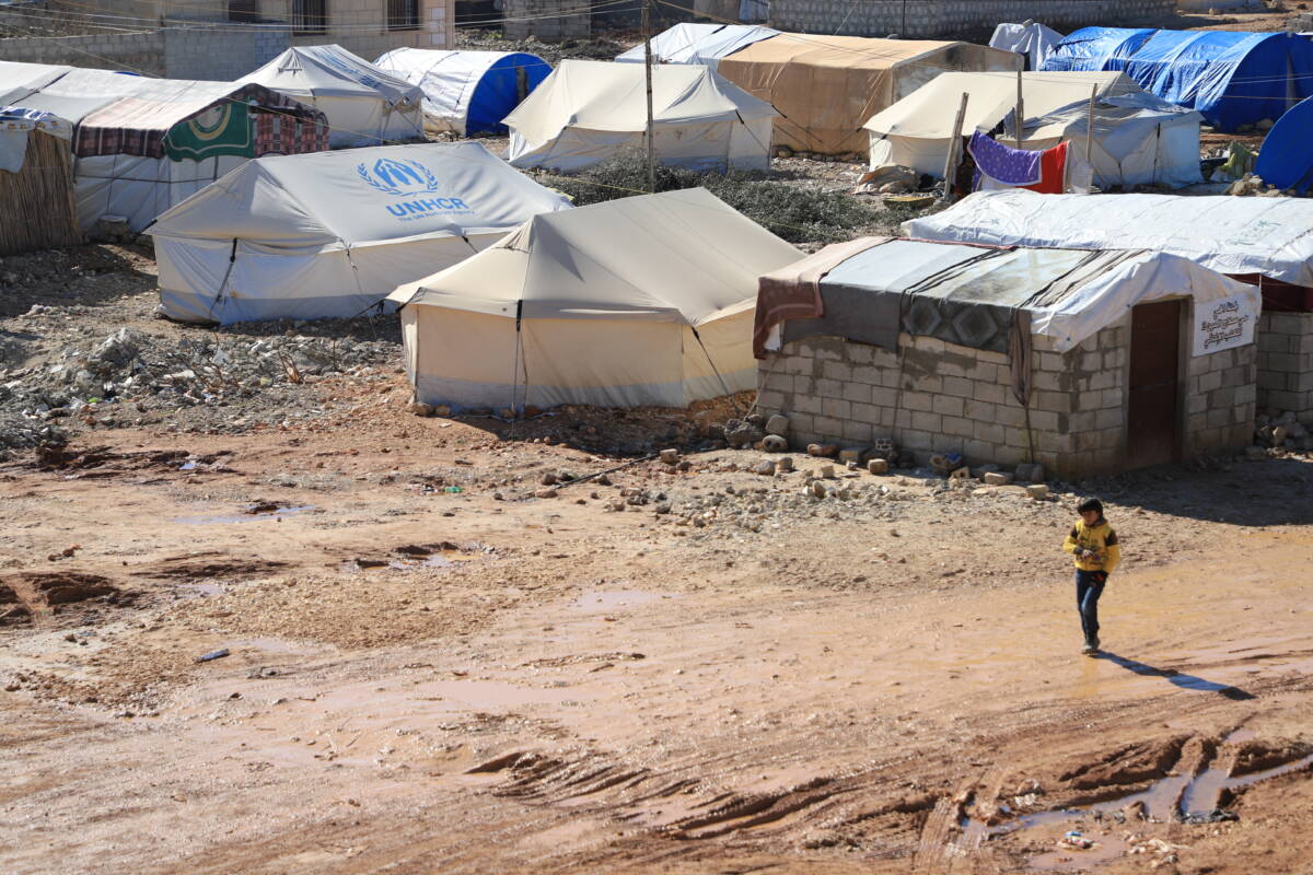 طفل يمشي في أحد مخيمات النازحين في ناحية جنديرس بمنطقة عفرين في ريف حلب الشمالي، وهي من المناطق الأكثر تضرراً بزلزال السادس من شباط/ فبراير من العام الماضي، 27/ 01/ 2024، (عبد المجيد القرح/ سوريا على طول) 