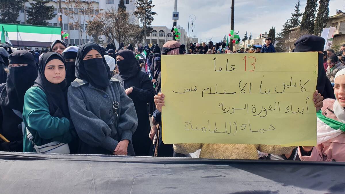 Women in northwestern Syria’s opposition-held Idlib city participate in a demonstration marking the 13th anniversary of the Syrian revolution. One woman, displaced from the Hama province city of al-Latamna, holds a sign that reads: “Surrender does not suit us, for we are the children of the Syrian revolution,” 15/3/2024 (Abd Almajed Alkarh/Syria Direct)