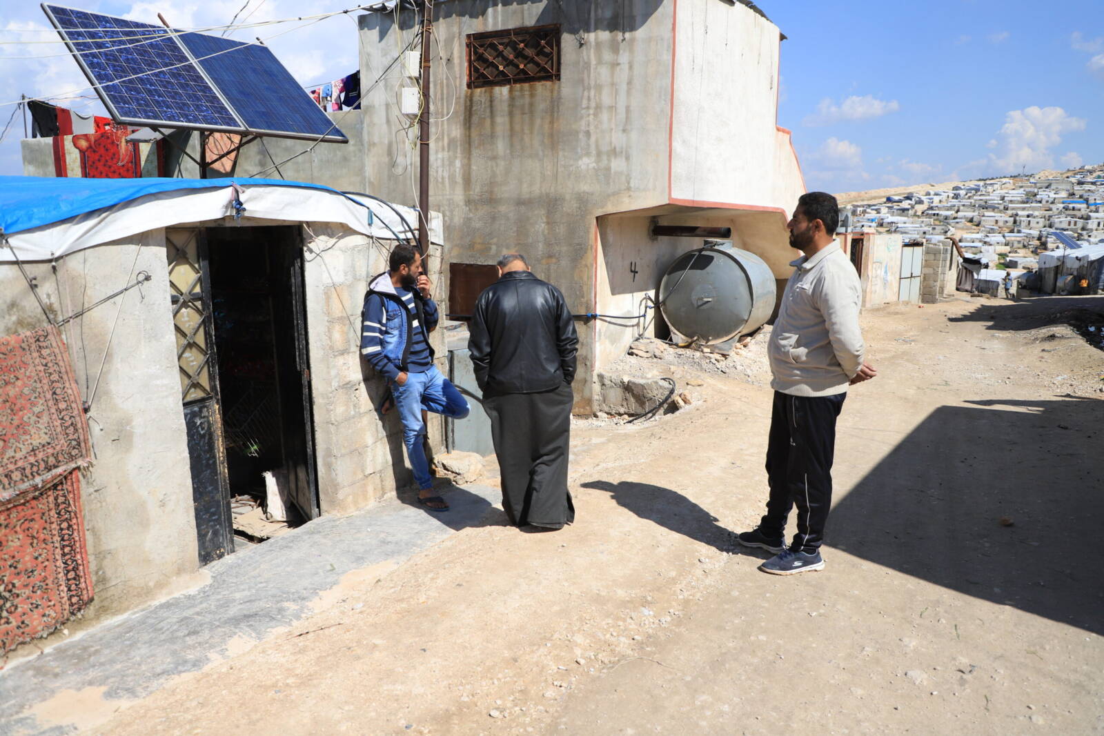 Mazen al-Wared, 40, stands with two of his neighbors in a neighborhood of Atma’s Umm al-Shuhada camp, 10/3/2024 (Abd Almajed Alkarh/Syria Direct)