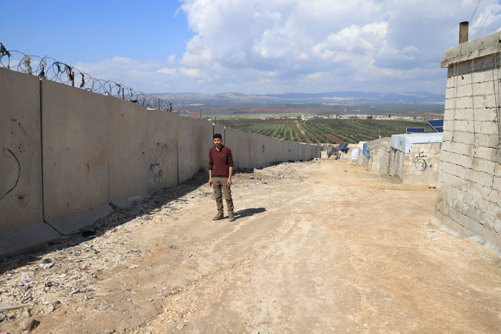 إبراهيم اليوسف، مدير مخيم الجزيرة، يقف إلى جانب الجدار الحدودي التركي، 10/ 03/ 2024 (عبد المجيد العمر/ سوريا على طول)