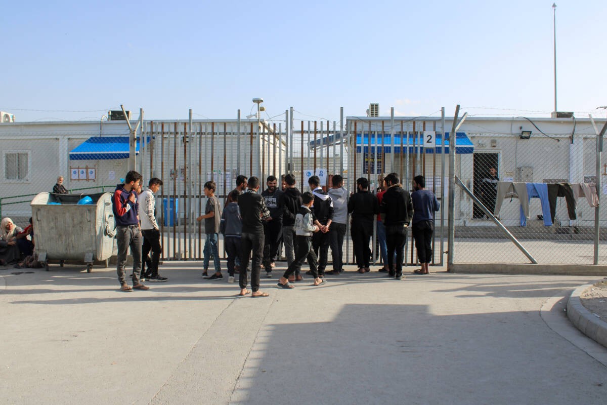 Young men, mostly Syrians, stand outside a gate at the Pournara Emergency Reception Center in Cyprus, 27/03/2024 (Hanna Davis/Syria Direct)
