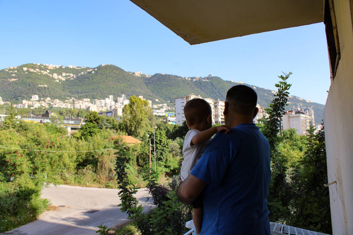 Basil Hussein al-Batoush, 35, holds his youngest child on the balcony of their new apartment in Jounieh, roughly a month after municipal police evicted them and other Syrians from an apartment complex in the Lebanese coastal city, 9/5/2024 (Hanna Davis/Syria Direct)
