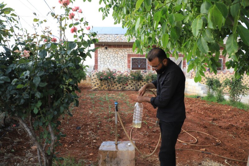 Samer al-Bakour, from al-Hebat village, fills a bottle from a spigot in his home’s garden, showing the change in the color of the water due to bacterial contamination, 27/5/2024 (Abd Almajed Alkarh/Syria Direct)